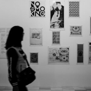 grayscale photo of woman in long sleeve shirt standing in front of wall with wall mounted